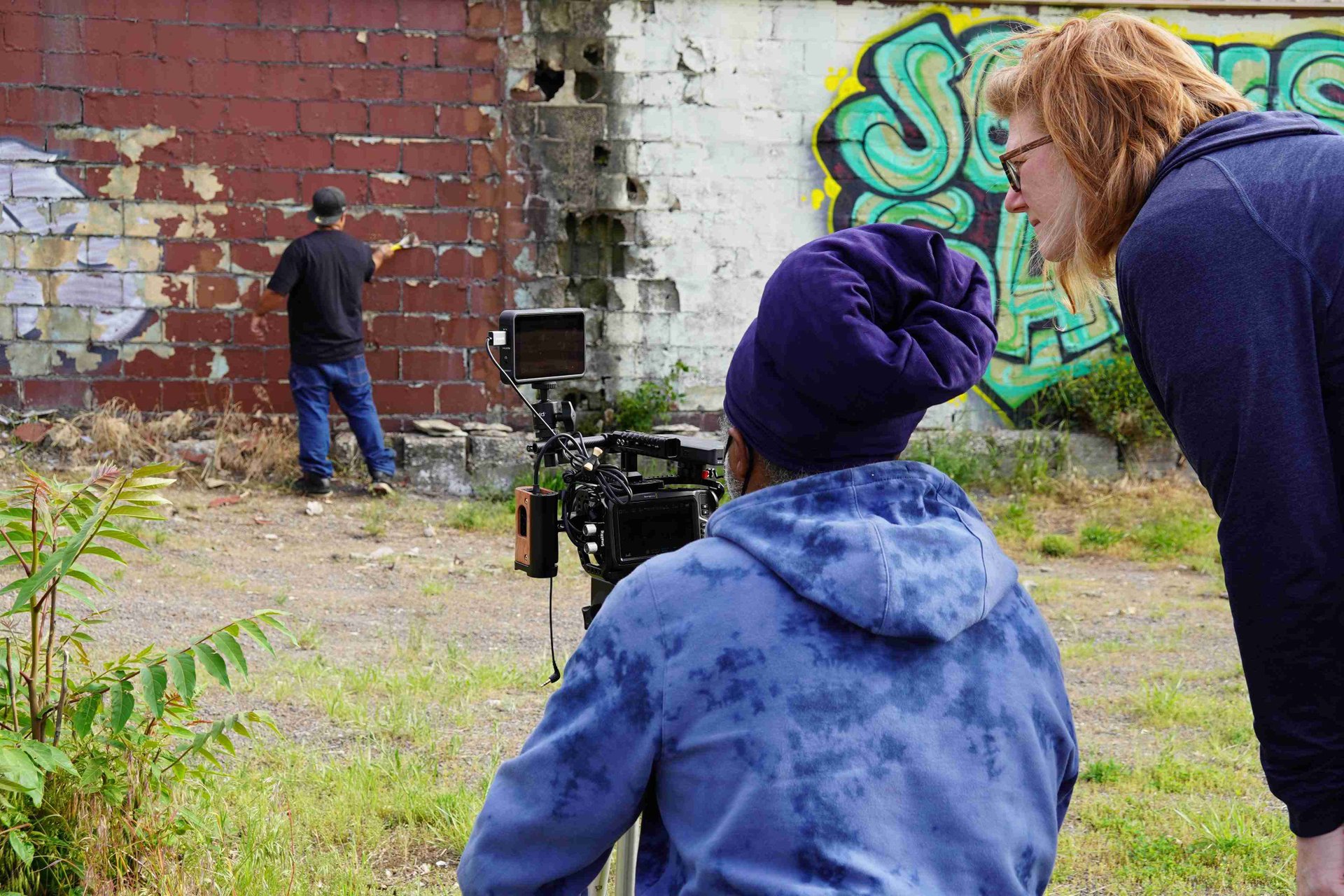 producers behind a camera, one man restoring a brick wall in front of the camera being filmed